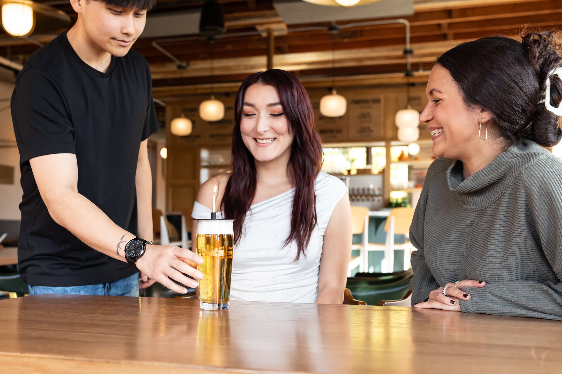 Person serving a birthday beer drink to two people at a bar.