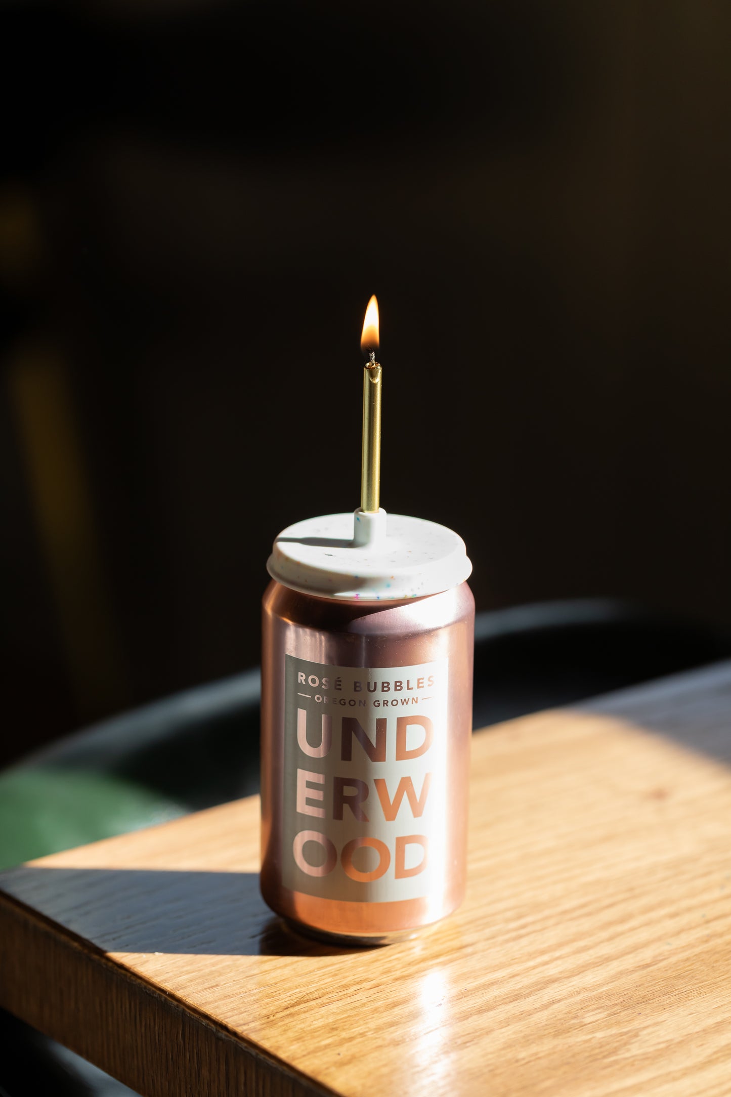 Candle on a canned beverage labeled 'Underwood' wine on a wooden surface with a dark background