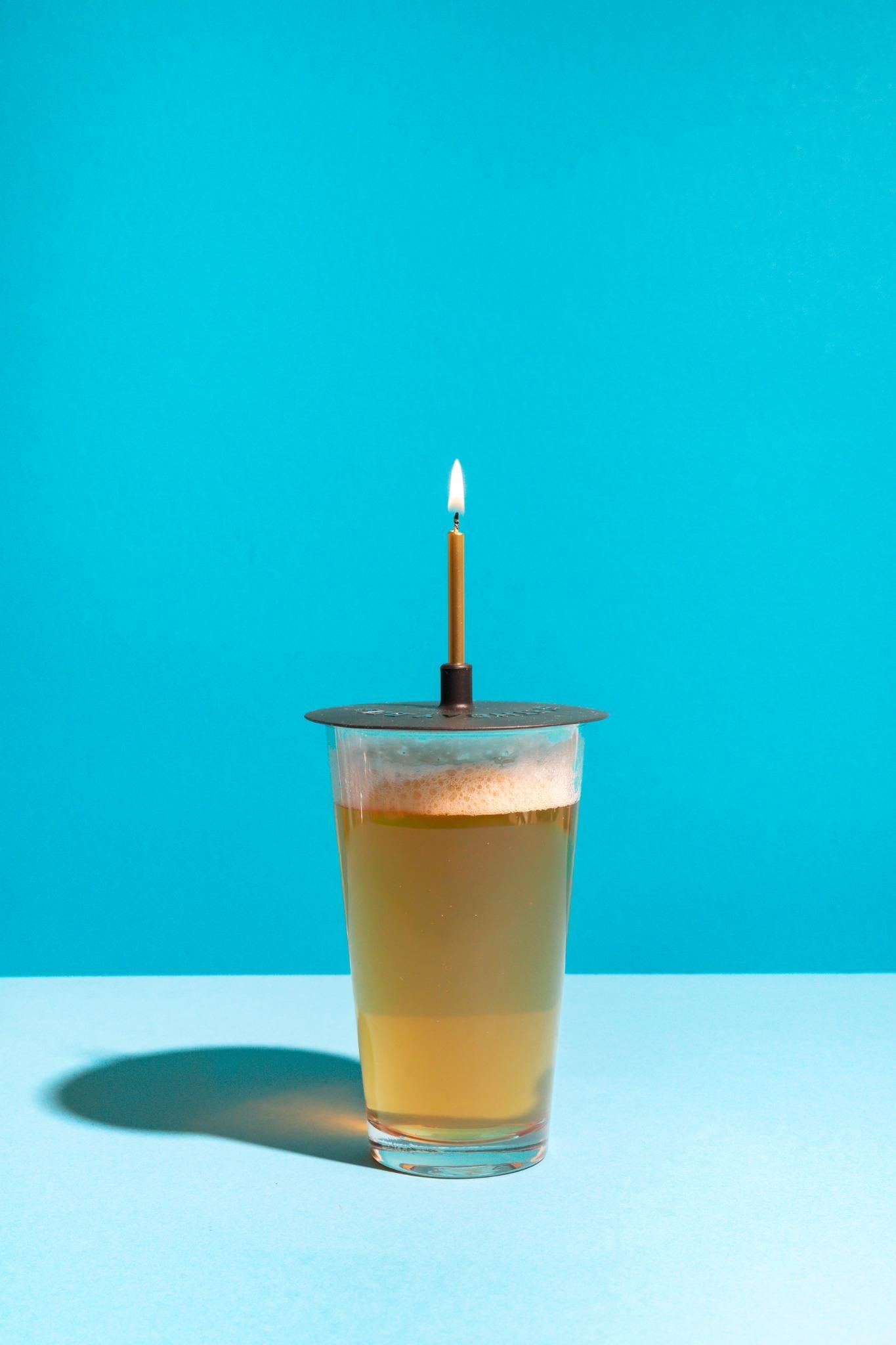 Glass of beer with a lit candle on a blue background